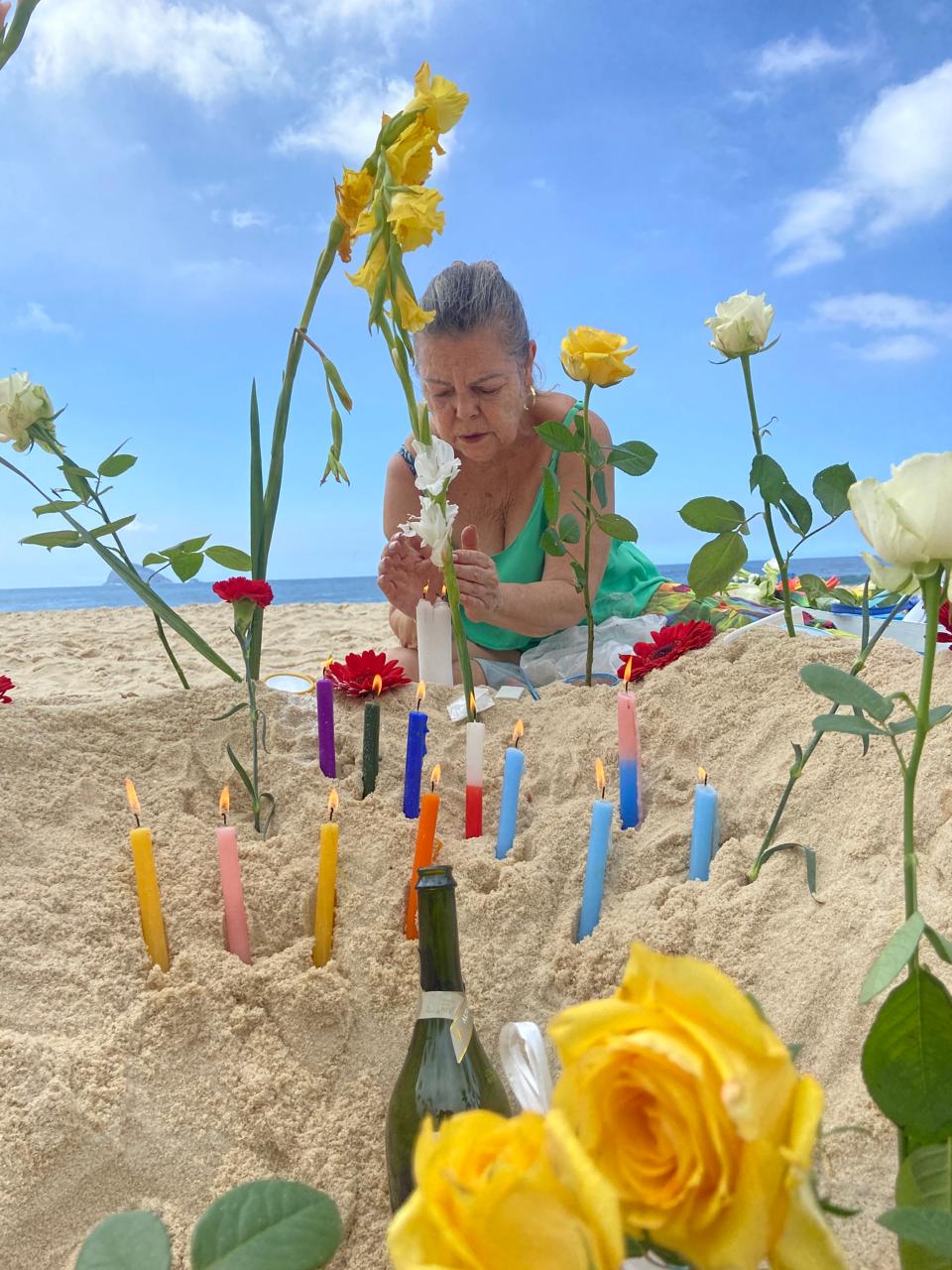 Velas e flores amarelas em ritual à beira-mar