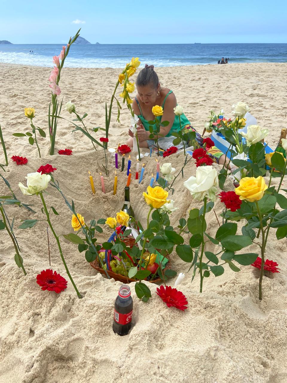 Oferenda com flores e velas na areia da praia