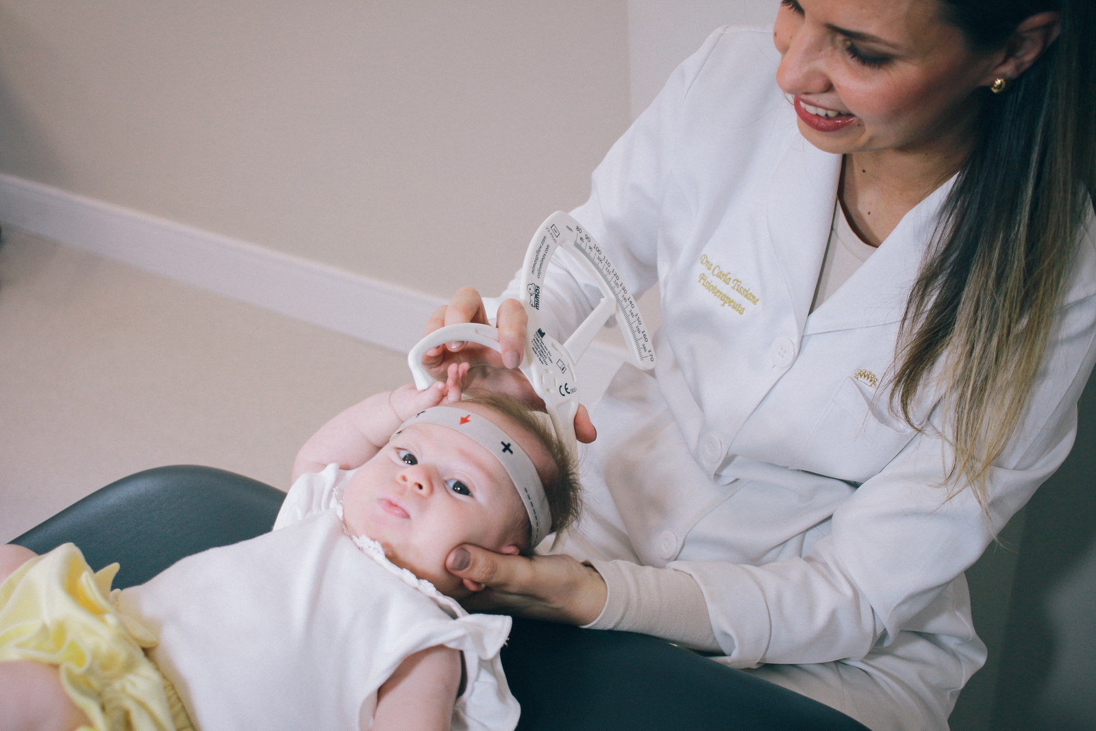 Dra. Carla Tissiane mede a cabeça de um bebê com craniômetro durante a avaliação.