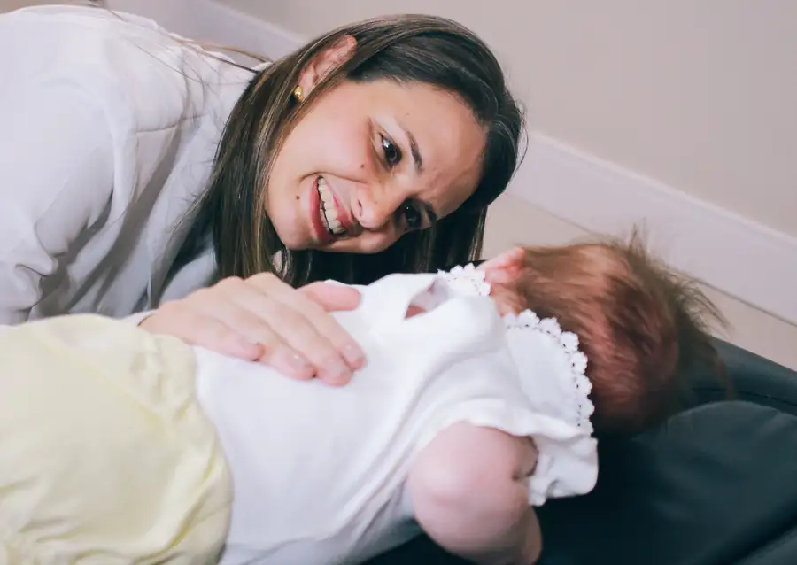Dra. Carla Tissiane sorri para um bebê deitado na maca durante a avaliação.