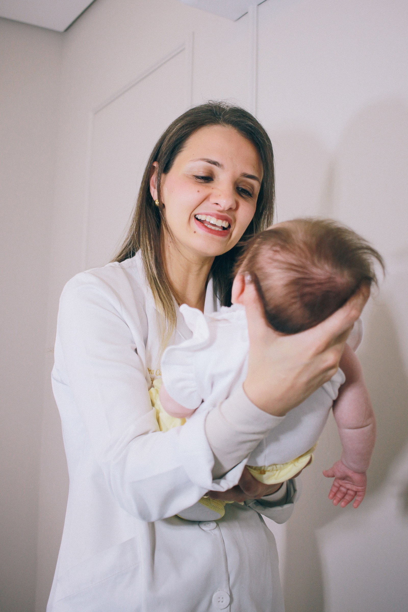 Dra. Carla Tissiane sorrindo, de jaleco, com um bebê no colo.